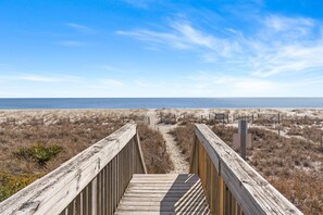A wooden boardwalk leading to a beach with a clear sky.