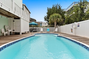 Piscina con plataforma de madera, rodeada de cercas blancas y sillas.