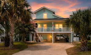 A two-story house with a balcony, surrounded by palm trees and a well-maintained lawn.