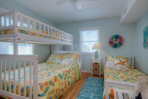 A child's bedroom with bunk beds, a window with blinds, a nightstand with a lamp, and a wall decoration.