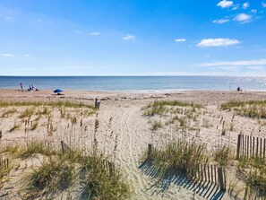 A beach with sand dunes, a clear sky, and a calm sea.