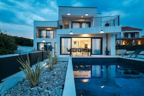 Ein modernes, zweistöckiges Haus mit Pool, Sitzgelegenheiten im Freien und Essbereich.