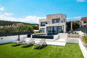 Ein modernes, zweistöckiges Haus mit Pool, Sitzgelegenheiten im Freien und Blick auf die Umgebung.