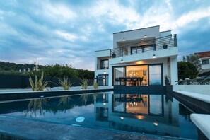 Ein modernes, zweistöckiges Haus mit Pool im Vordergrund.