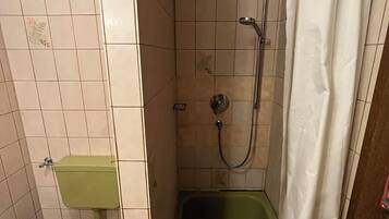 Ein kleines Badezimmer mit Toilette, einer Duschkabine mit Vorhang und einer grünen Badewanne.