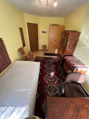 A room with a bed, a wooden cabinet, a chair, and a patterned rug.