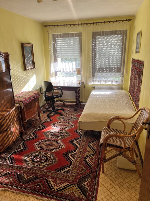 A room with a bed, a desk, a chair, a dresser, and a patterned rug.