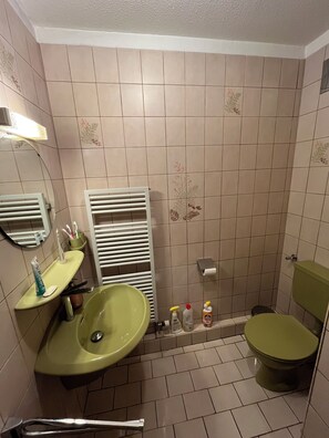 A bathroom with a green sink, a toilet, and a shower area.
