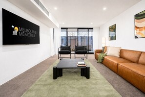 A modern living room with a flat-screen TV, two black chairs, a brown leather sofa, and a green rug. - The Richmond Grand | Near MCG + 3 Free Car Spaces (Richmond)
