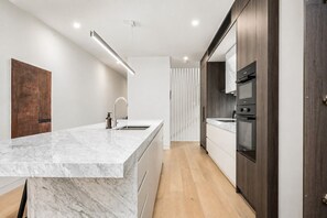 A modern kitchen with a marble countertop, stainless steel appliances, and wooden cabinetry. - The Richmond Grand | Near MCG + 3 Free Car Spaces (Richmond)