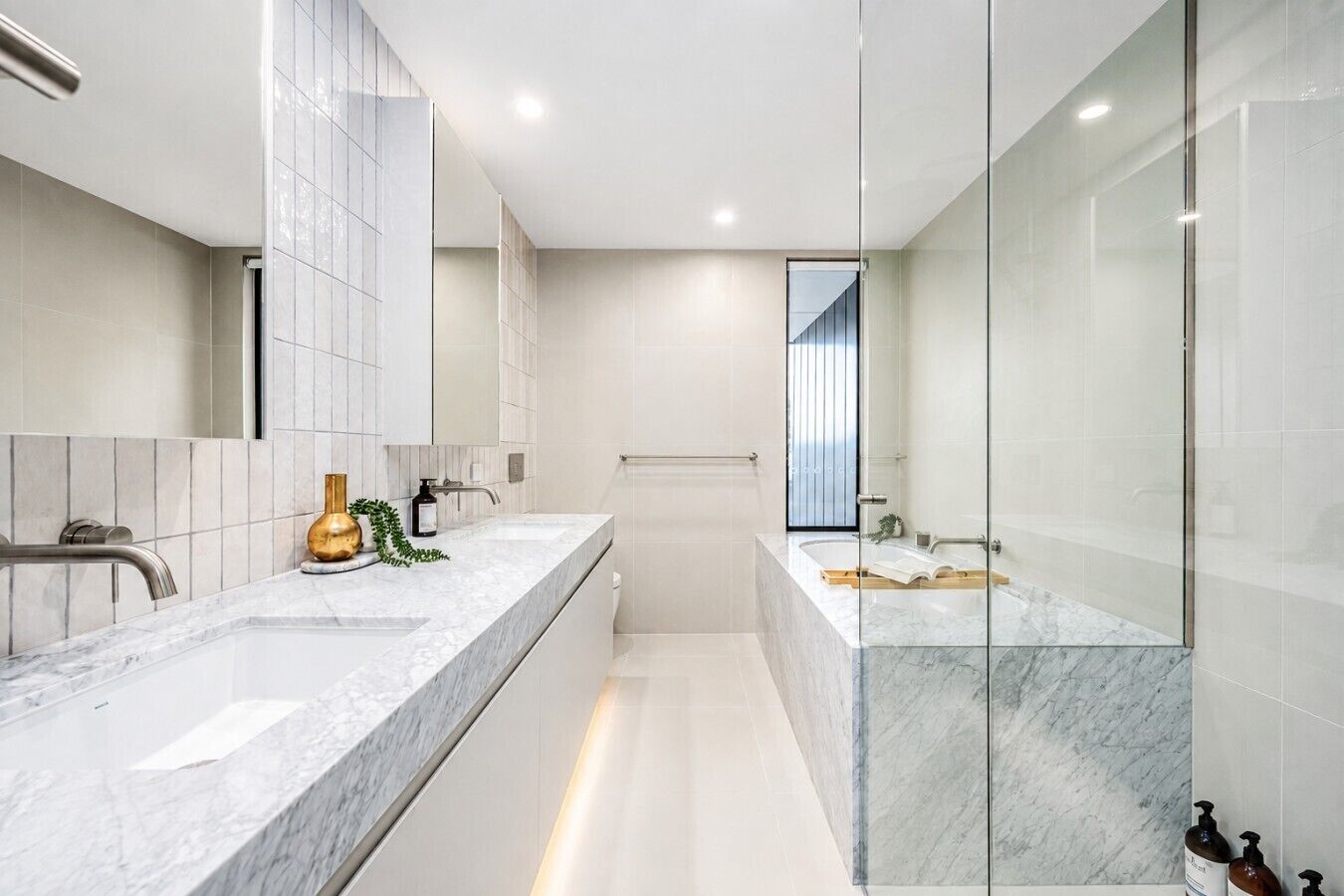 A modern bathroom with a marble vanity, a glass shower enclosure, and a large mirror.