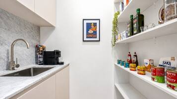 A modern kitchen with a built-in espresso machine, a sink, and shelves stocked with canned goods and condiments.