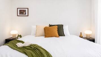 A neatly made bed with a green throw blanket, two bedside lamps, and a framed picture on the wall.