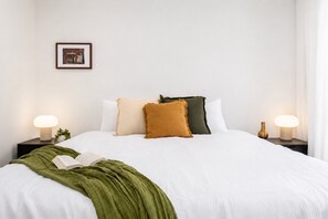 Ein ordentlich bezogenes Bett mit einer grünen Tagesdecke, zwei Nachttischlampen und einem gerahmten Bild an der Wand.