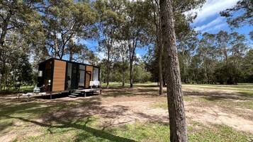 A mobile home with a deck, situated in a grassy area with trees.