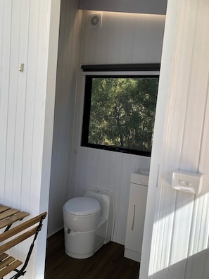 Baño pequeño con inodoro, lavamanos y ventana que da a árboles.