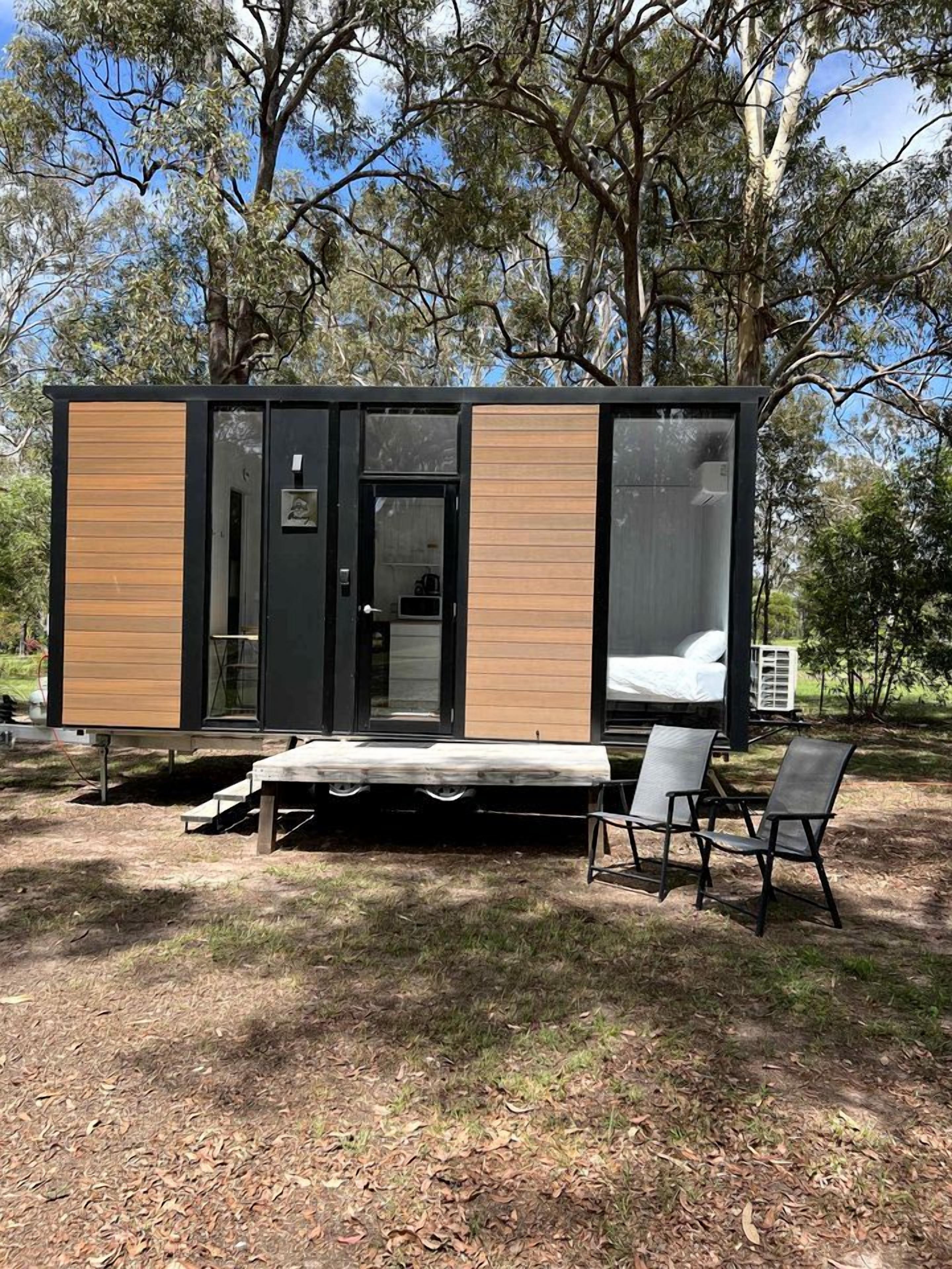 Une cabane moderne comprenant un lit, un petit coin cuisine et un espace salon avec des chaises.