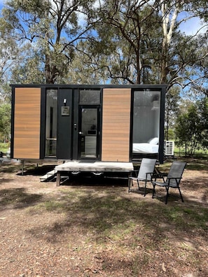 Una cabaña moderna con una cama, un pequeño rincón de cocina y una zona de estar con sillones.