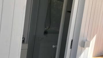 A glass-enclosed shower area with a showerhead and control panel, adjacent to a white wall with a door.