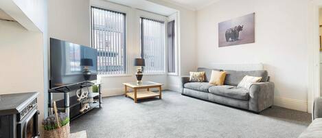 A modern living room with a flat-screen TV, a grey sofa, and a coffee table.