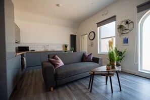 Een moderne woonruimte met een grijze bank, een klein rond tafeltje en een keukenhoek met een magnetron.