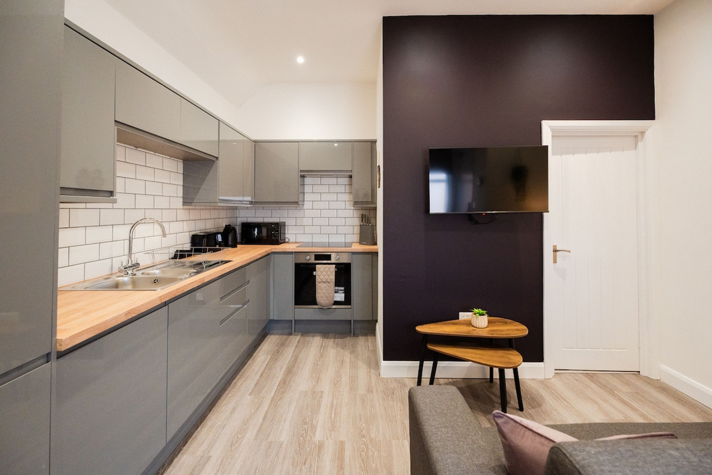 A modern kitchen with grey cabinets, a wooden countertop, and a built-in oven.