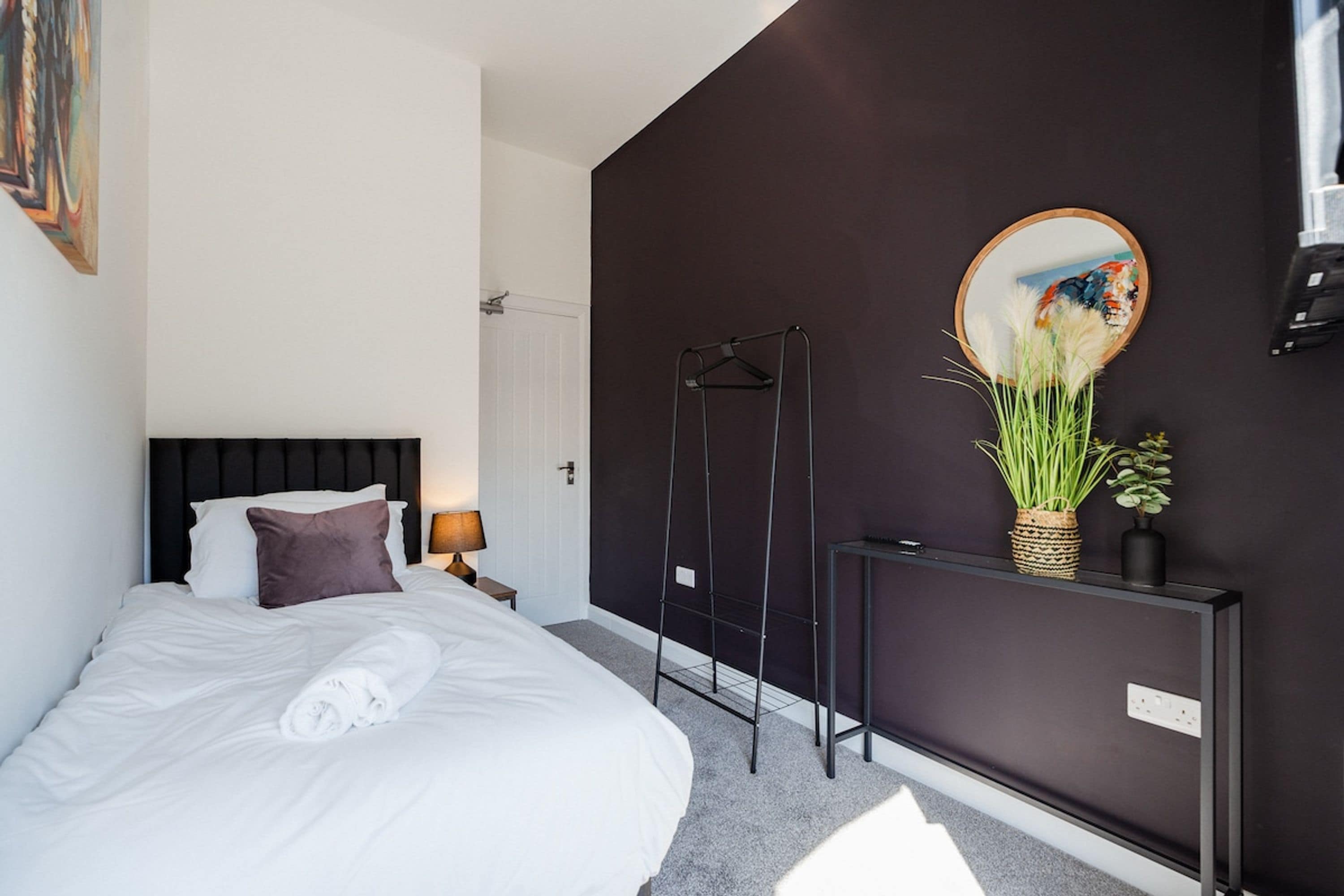 Une chambre d’hôtel moderne équipée d’un lit, d’une table de chevet avec une lampe, d’un téléviseur fixé au mur et d’un miroir.