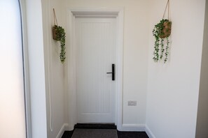 Un couloir avec une porte blanche, une poignée de porte noire et deux paniers suspendus contenant des plantes vertes.