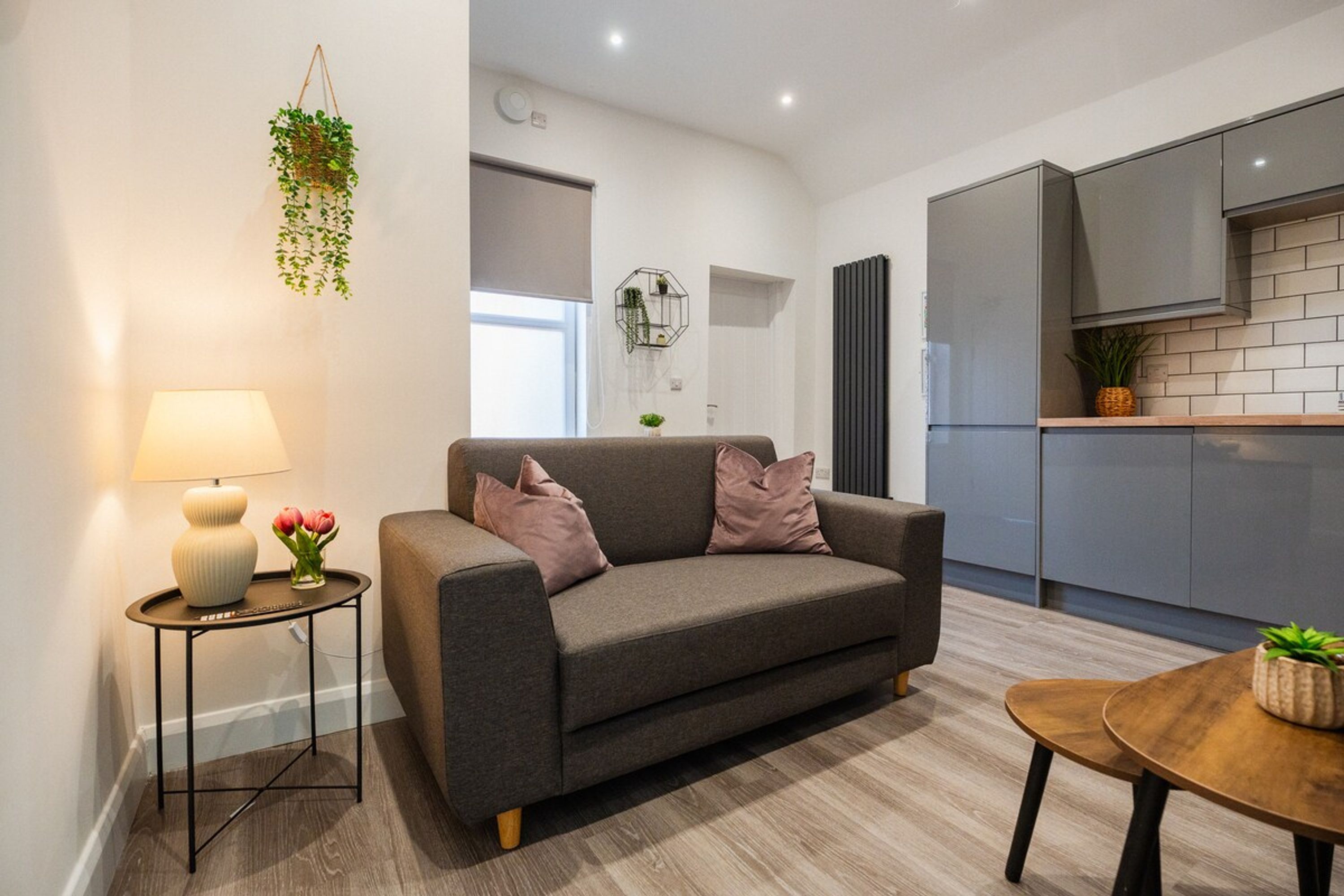 Ein modernes Wohnzimmer mit einem grauen Sofa, einem kleinen Beistelltisch mit einer Lampe und einem Holztisch.