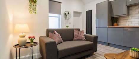 A modern living room with a grey sofa, a small side table with a lamp, and a wooden coffee table.