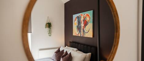 A bedroom with a bed, pillows, a hanging plant, and a painting of an elephant.