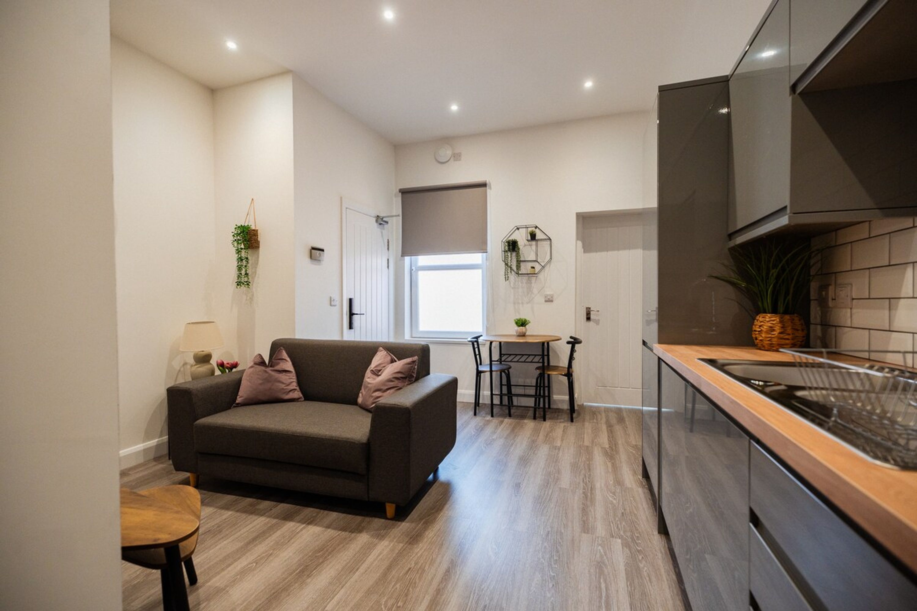 A modern kitchen with a built-in oven, a dining area with a table and chairs, and a living space with a sofa and a small table.