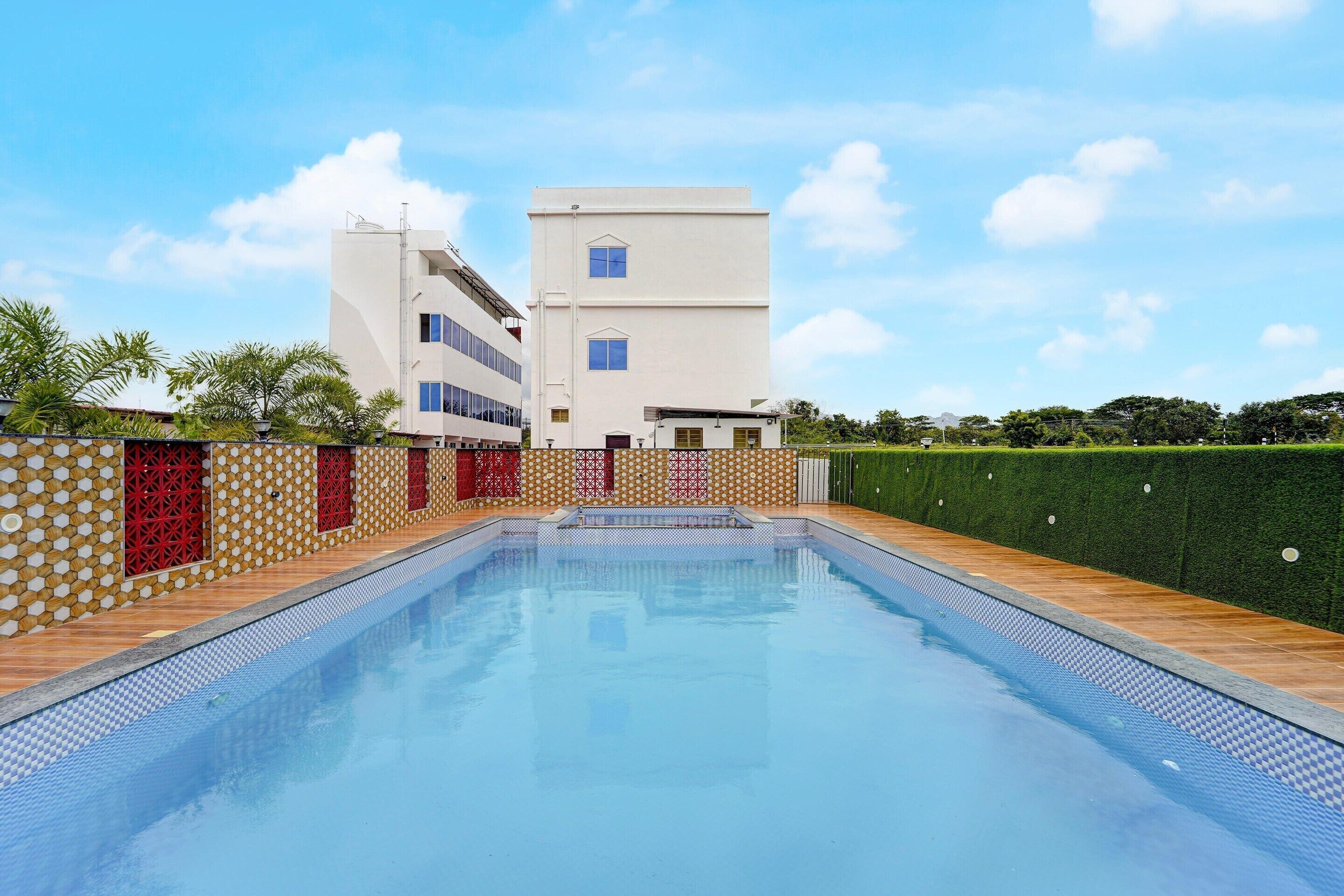 A swimming pool with a tiled edge, surrounded by a patterned wall and a hedge.