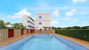 Una piscina con borde de azulejos, rodeada por un muro decorativo y un seto.