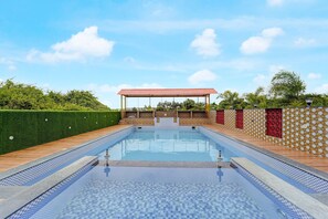 A swimming pool with a tiled deck, surrounded by a low wall with patterned tiles and a pergola with a red roof. - Classic Sonia Mahi Inn (Nagercoil)