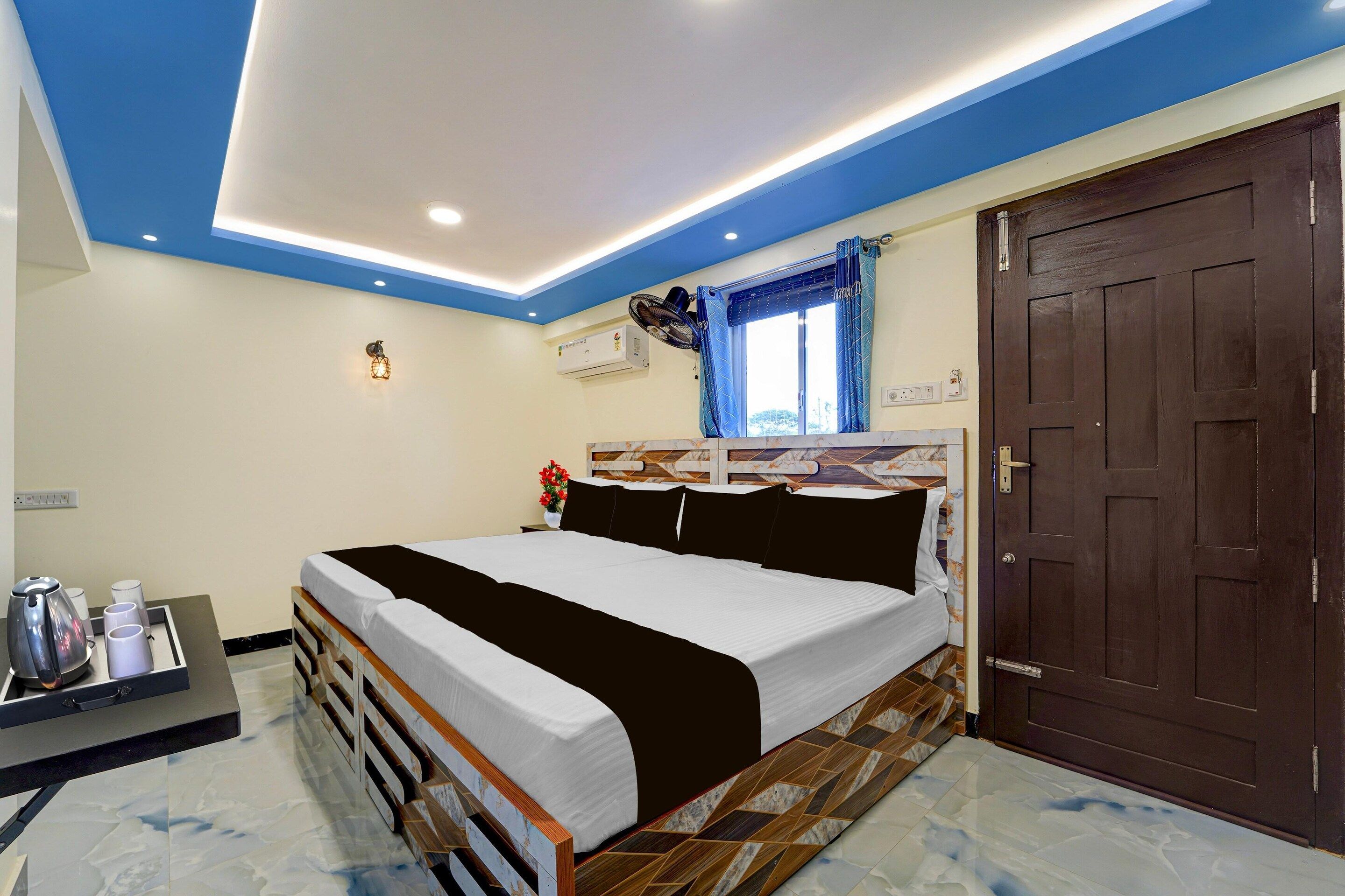 A bedroom with a bed, a nightstand, a window with curtains, a door, and an air conditioning unit.