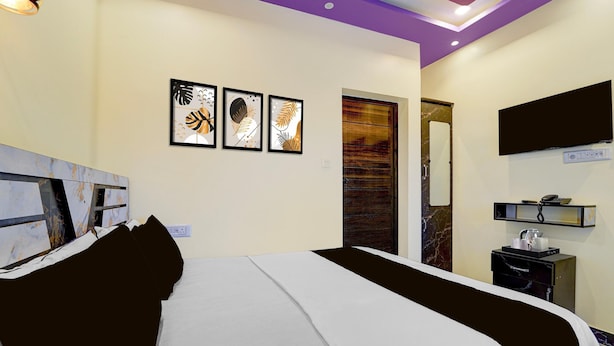 Una habitación de hotel con una cama, un televisor montado en la pared y una obra de arte sobre la cama.