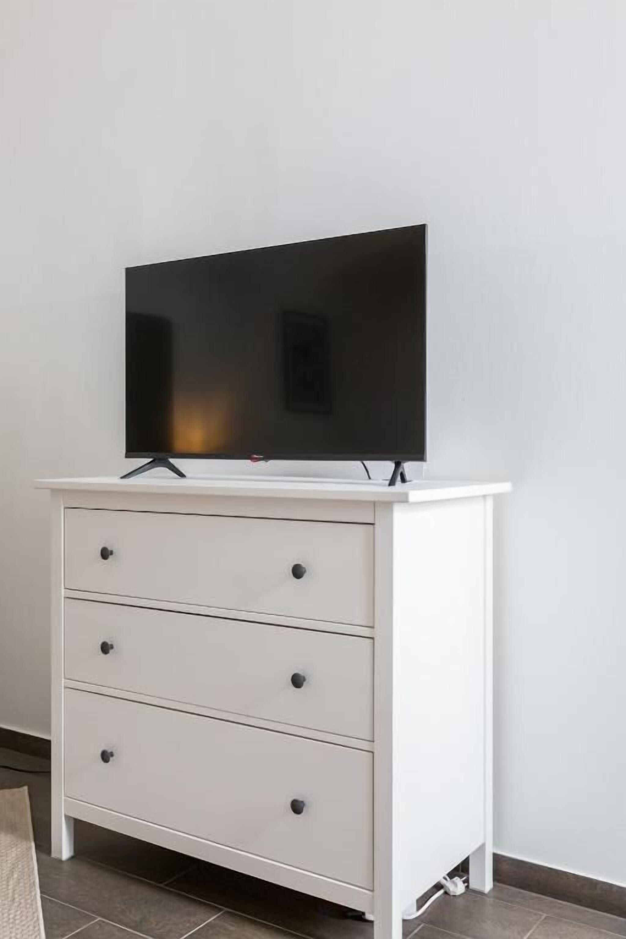 Eine weiße Kommode mit einem Flachbildfernseher darauf, Schubladen und einer Kabelmanagement-Lösung.