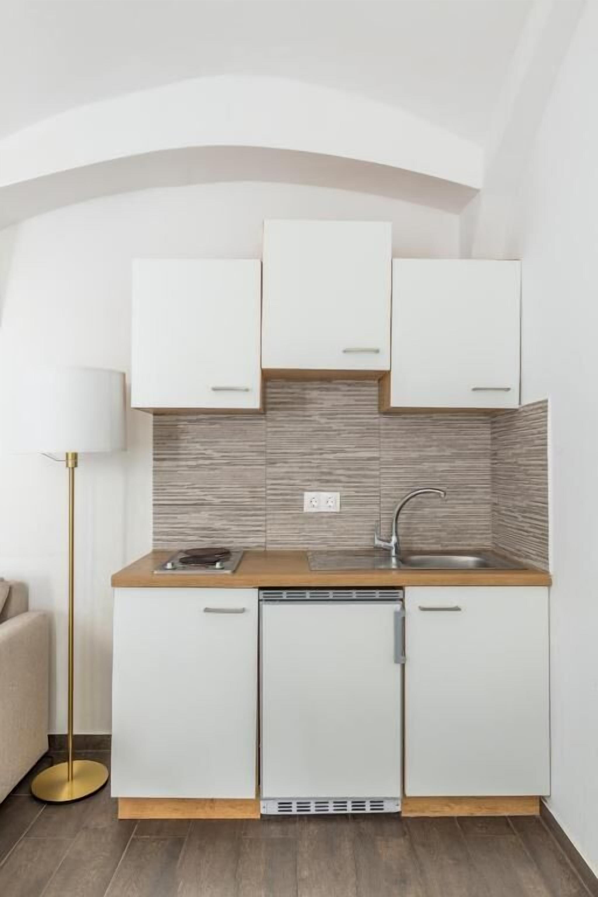 Een kleine keuken met witte kastjes, een houten aanrechtblad en een inbouw vaatwasser.