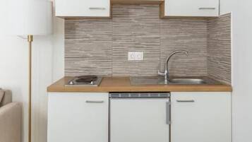 Een kleine keuken met witte kastjes, een houten aanrechtblad en een inbouw vaatwasser.