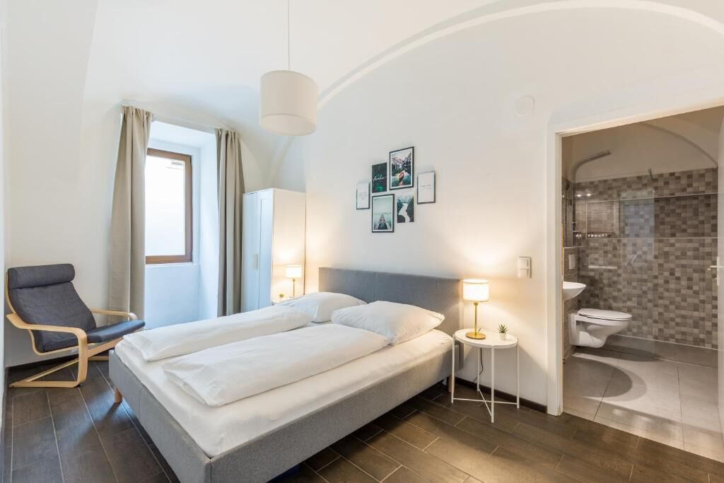 Une chambre d’hôtel comprenant un lit, une chaise, une table de chevet, une lampe et un espace douche.