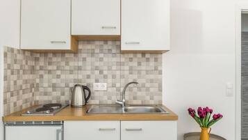A modern kitchen with white cabinets, a tiled backsplash, a stainless steel kettle, and a small round table with a vase of flowers.