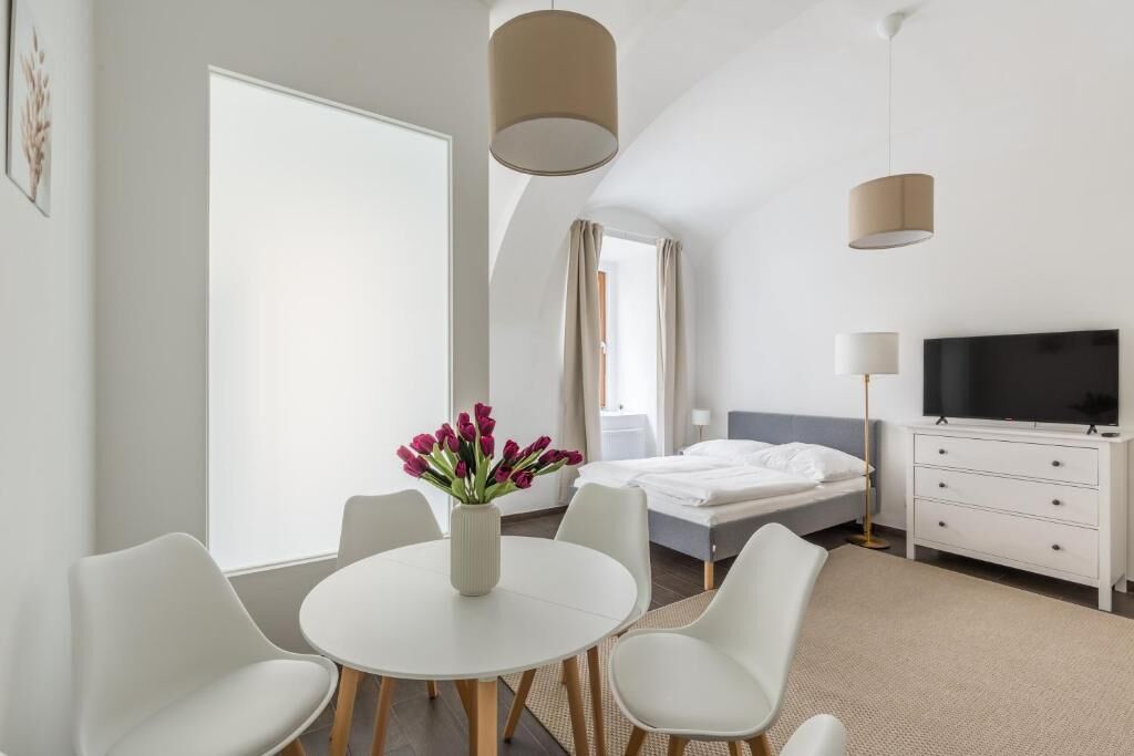 Een moderne hotelkamer met een bed, een televisie, een bureau met stoelen en een bloemenvaas.