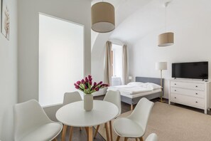Habitació d'hotel moderna amb un llit, una televisió, una taula de treball i cadires, i un ram de flors.