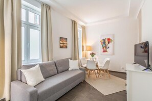 Una sala de estar moderna con un sofá gris, sillas blancas, una mesita y obras de arte en las paredes.