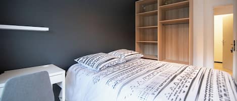 A bedroom with a bed, a desk, and a wardrobe.