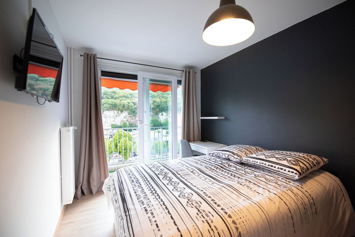 A bedroom with a bed, a TV mounted on the wall, and a window with curtains.