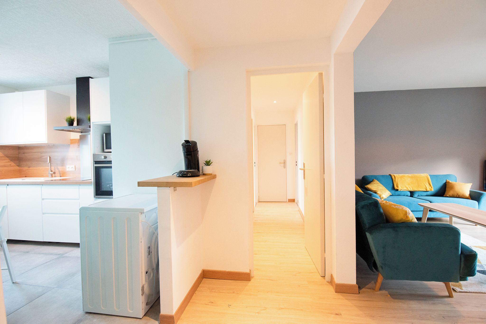 Een modern appartement met een keuken, een woonkamer met een blauwe bank en een gang die naar een andere kamer leidt.