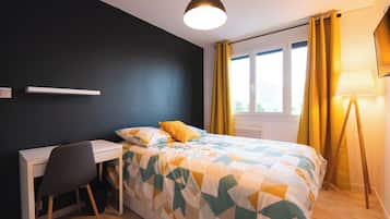 A bedroom with a bed, a desk, a chair, a lamp, and a window with curtains.