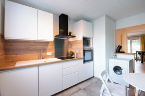 A modern kitchen with white cabinets, a wooden countertop, a built-in oven, and a washing machine. - Les chambres du Vercors (Fontaine)